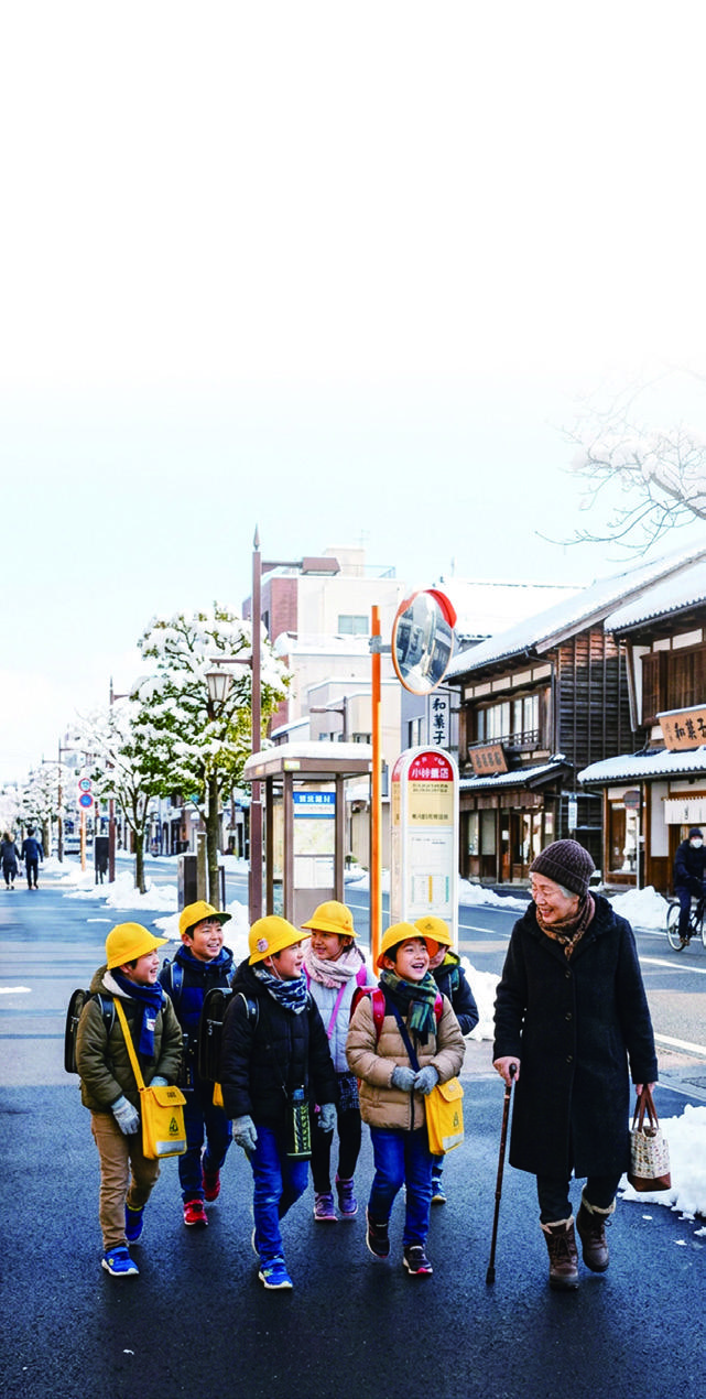 雪のある街並みを歩く子どもたちと高齢者